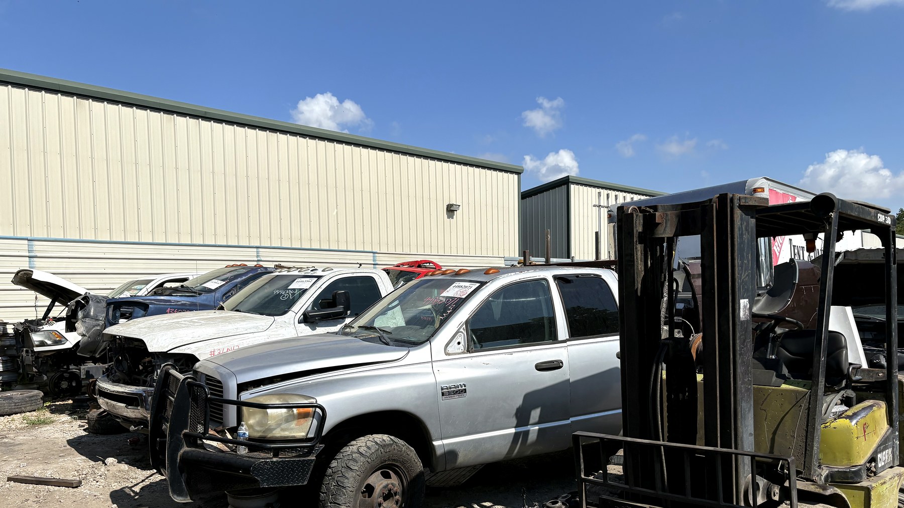 Parts yard forklift beside Dodge diesel trucks at NEXT Auto Parts